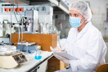 Attentive scientist engaged in research in chemical laboratory, noting results in test chart