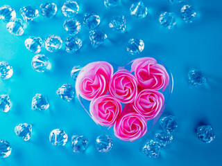A heart filled with pink roses is surrounded by gem stones, blue background. Concept of love and...