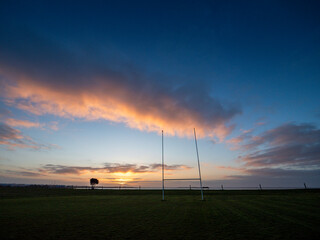 Silhouette of a tall goal posts and palm tree in a field against dramatic sunrise sky. National...