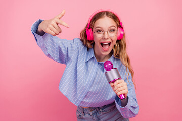 Cheerful young woman with a pink microphone and headphones smiling enthusiastically against a...