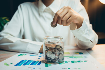 Concept of saving money. Close-Up of Person Depositing Coins into Glass Jar on Table with Financial...