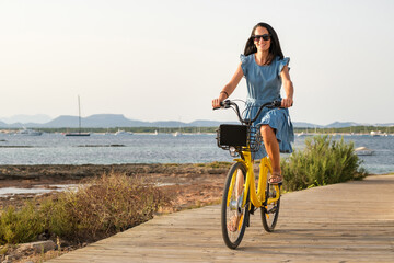 Cheerful woman riding bicycle along embankment near sea