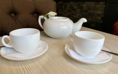 a white teapot with tea and two mugs are on the table