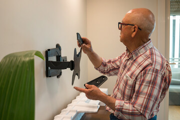 Elderly man installing a TV bracket on a wall