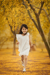 Happy little girl in white dress running in the park along  the blooming yellow trees, childhood memories and active kids concept