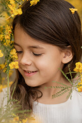 Closeup spring or summer portrait of little smiling girl with blooming yellow flowers, childhood memories and happy kids portrait