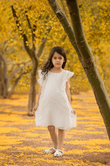 Spring and summer portrait of little girl in white dress around blooming yellow trees at kindergarten age