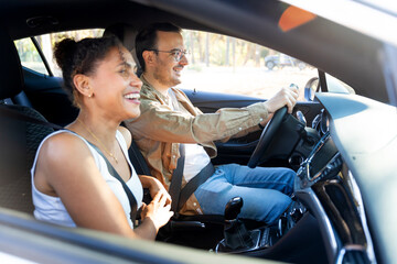 Happy latin couple enjoying road trip, driving modern car on vacation