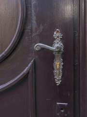 Part of the door, dark in color, with a very beautiful handle, of a special shape