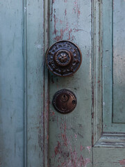 Part of an old wooden door, light in color, with a metal handle