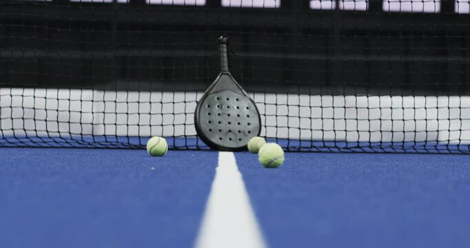 Padel racket and balls on indoor court near net, ready for match, copy space
