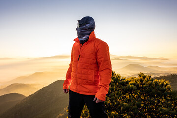 Mountain adventurer in orange jacket enjoying sunrise view