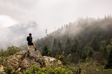 Back view of an unrecognizable male hiker on a rock in a foggy forest