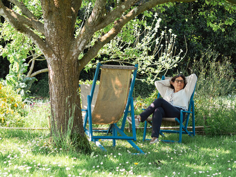 Senior woman relaxing on garden deck chair under tree