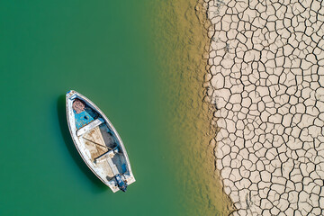 A small boat rests on a body of water next to drought-stricken land, highlighting environmental concerns and the impact of climate change.