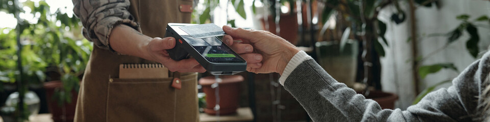 Image showing a senior making contactless payment in a greenhouse with a card reader. The scene...