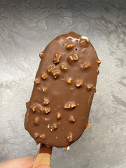 Delicious chocolate-covered ice cream bar with crunchy nuts held in hand against a light backdrop