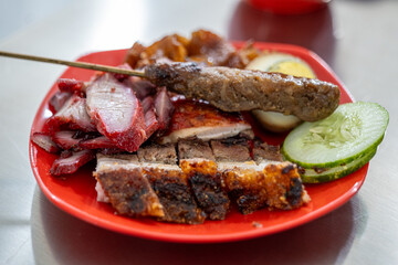 The menu at a Chinese restaurant consists of roast pork, pork char siu, sausage, pig ears, skin, eggs, and pork satay. With cucumber slices.