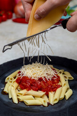 Putting grated parmesan cheese on top of penne pasta with red sauce