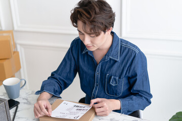 Startup small business owner work with computer at home. Young Asian man freelance preparing delivery parcel on table. Ecommerce dropshipping, SME ecommerce concept. Online marketing packaging.