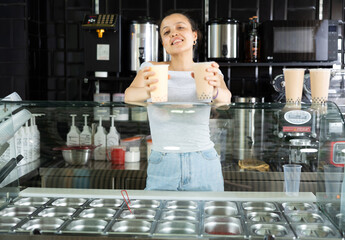 Young woman holding out plastic cups of bubble tea in cafe