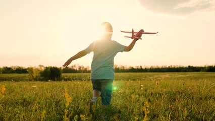 Young boy pilot is flying an airplane over verdant field. Joyful boy is playing with toy airplane...