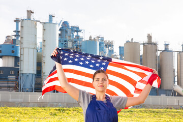 Calm young woman worker posing with the USA flag in hands against background of factory