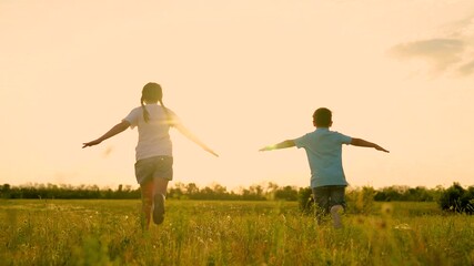 Happy boy and girl kids running on meadow with open hands flying imagination slow motion. Cheerful children speed movement on field sunset sky imagine aviation pilot jet flight freedom back view