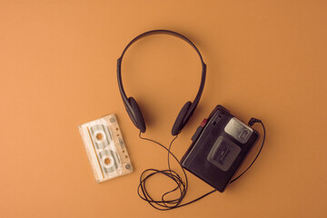 Classic cassette player, headphones, and tape on brown background spark warm memories of the 90s. Large copy space for any project.