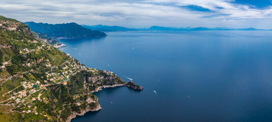 Aerial view of the Amalfi Coast in Italy, featuring cliffs, terraced hills, charming buildings, boats on the Tyrrhenian Sea, and distant mountains.