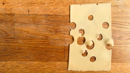 Hole-riddled Swiss cheese slice on rustic wood, evoking Emmentaler delicacies and La Fete du...