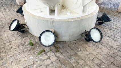 Floodlights encircle a weathered monument pedestal, evoking urban exploration vibes, light art...