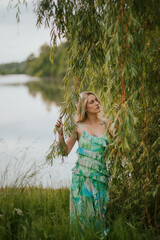 Fototapeta premium Dreamy Woman by the Willow Tree in Flowing Green Dress Near Water