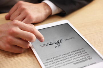 Electronic signature. Man using tablet at wooden table, closeup