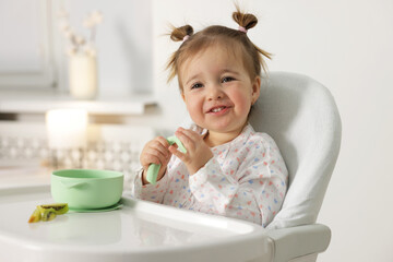 Cute little baby eating healthy food in high chair indoors