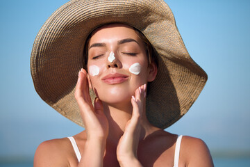 Plakat Beautiful woman with sun protection cream on face at beach. Skin care. Beautiful Woman In Bikini apply sunscreen on skin.