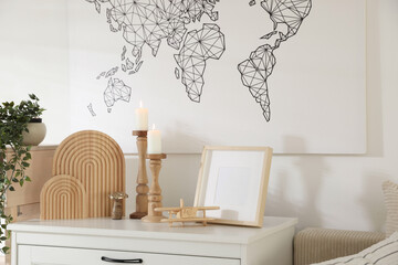 Stylish candlesticks with burning candles and other decor on cabinet near wall indoors