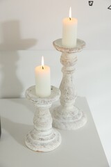 Stylish candlesticks with burning candles on table near white wall indoors, closeup