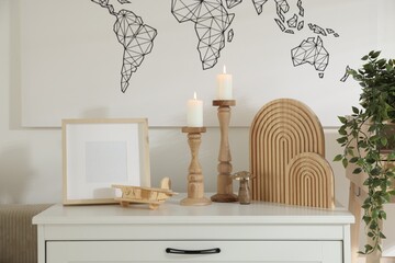 Stylish candlesticks with burning candles and other decor on cabinet near wall indoors