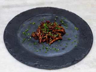 Shimeji mushroom served with chives on black stone plate. Typical oriental meal. Detail of food dish, closeup, selective focus.