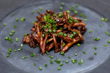 Shimeji mushroom served with chives on black stone plate. Typical oriental meal. Detail of food dish, closeup, selective focus.