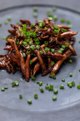 Shimeji mushroom served with chives on black stone plate. Typical oriental meal. Detail of food dish, closeup, selective focus.