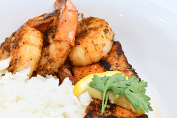 This image showcases a delicious meal featuring grilled shrimp, a perfectly seared salmon fillet topped with a fresh lemon slice and cilantro, accompanied by a serving of fluffy white rice.