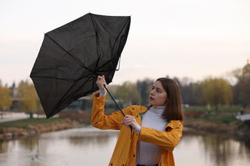 Teenage girl with broken umbrella fighting wind under rain outdoors