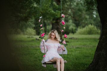 Woman in a Flowing Pink Dress Sitting on a Floral Swing in Nature