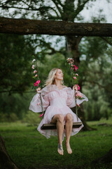 Woman in a Flowing Pink Dress Sitting on a Floral Swing in Nature