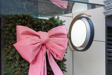 A large pink bow decorates a holiday scene with festive lights and green foliage, evoking holiday...