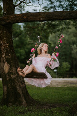 Woman in a Flowing Pink Dress Sitting on a Floral Swing in Nature