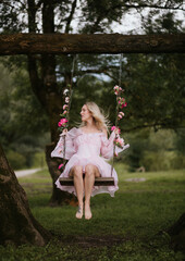 Woman in a Flowing Pink Dress Sitting on a Floral Swing in Nature