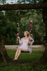 Woman in a Flowing Pink Dress Sitting on a Floral Swing in Nature